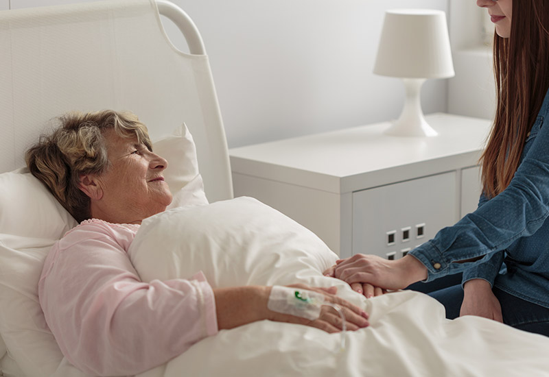 A hospice senior woman at Spring Lake Skilled Nursing & Rehabilitation in Shreveport, LA, lies in bed while her granddaughter visits.